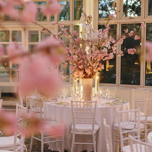 A large Pink Cherry Blooms centerpiece is at each dinner table for a wedding reception inside the Palm House. A large Pink Cherry Blooms centerpiece is at each dinner table for a wedding reception inside the Palm House.