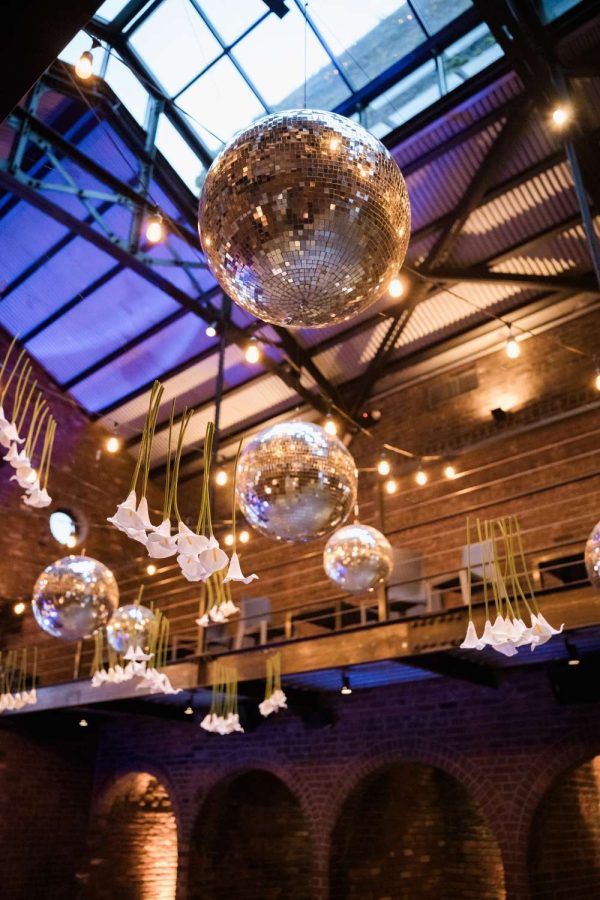Inside The Foundry's main reception room, string lights and multiple mirror balls hang from the ceiling. Additionally, Rose Hip Social provided the white calla lilies suspended overhead.