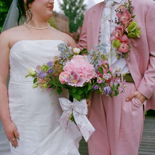 A couple wearing a white wedding dress and pink suit.