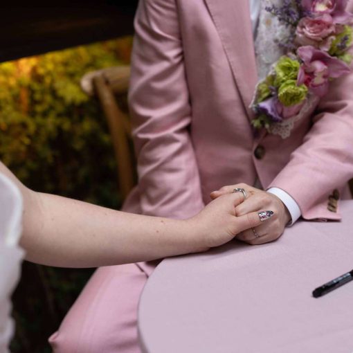 A couple wearing a white wedding dress and pink suit holding hands.