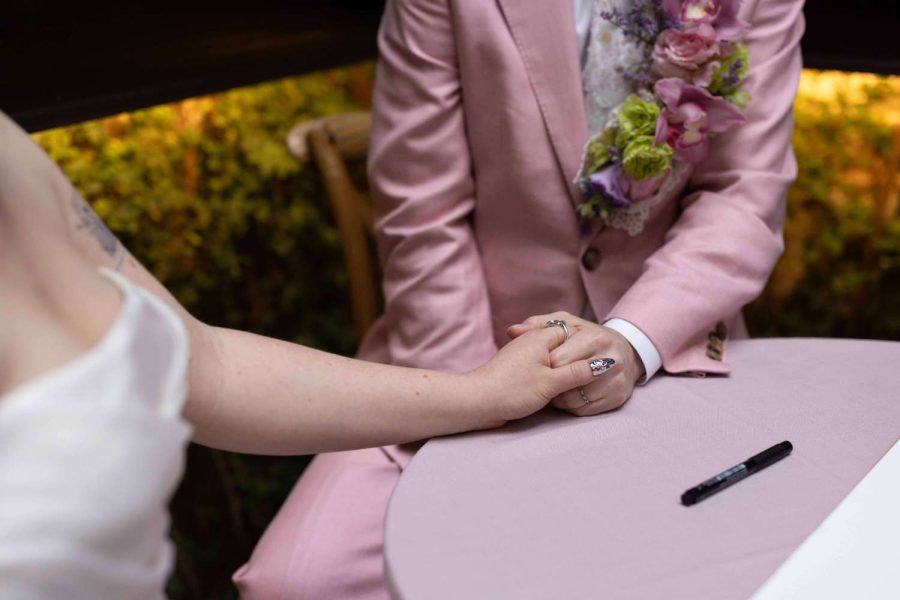 A couple wearing a white wedding dress and pink suit holding hands.
