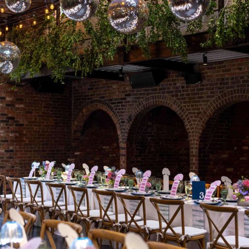A photo of a colorful indoor wedding reception featuring both colorful and lush green florals, along with String Lights and Multiple Disco Balls (Mirror Balls) hanging overhead at the Foundry in Long Island City, Queens, New York.