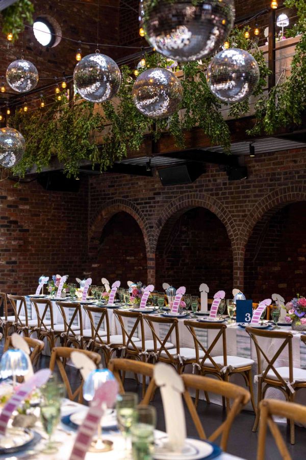A photo of colorful indoor wedding reception featuring both colorful and lush green florals, along with String Lights and Multiple Disco Balls (Mirror Balls) hanging overhead at the Foundry in Long Island City, Queens, New York.
