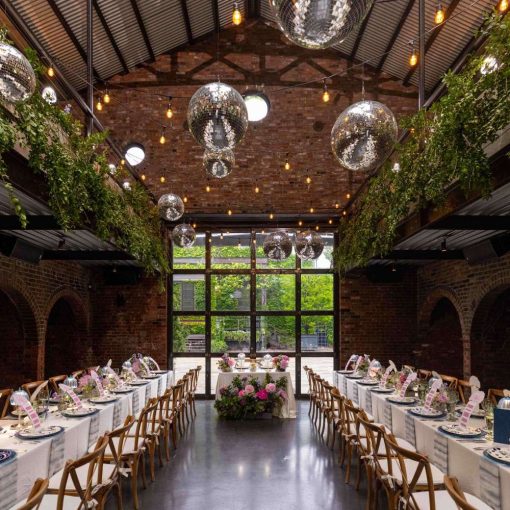A photo of a colorful indoor wedding reception featuring both colorful and lush green florals, along with String Lights and Multiple Disco Balls (Mirror Balls) hanging overhead at the Foundry in Long Island City, Queens, New York.