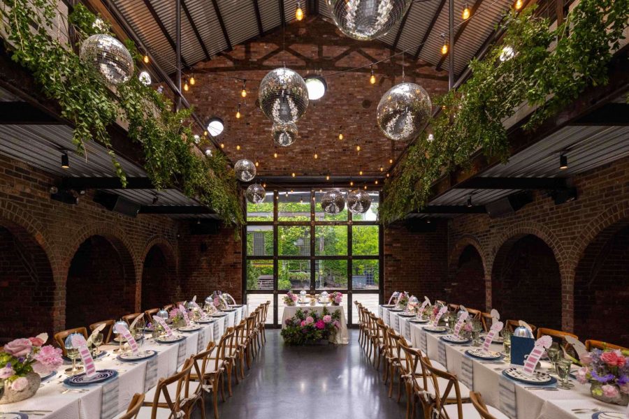 A photo of colorful indoor wedding reception featuring both colorful and lush green florals, along with String Lights and Multiple Disco Balls (Mirror Balls) hanging overhead at the Foundry in Long Island City, Queens, New York.