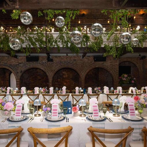 A photo of a colorful indoor wedding reception featuring both colorful and lush green florals, along with String Lights and Multiple Disco Balls (Mirror Balls) hanging overhead at the Foundry in Long Island City, Queens, New York.