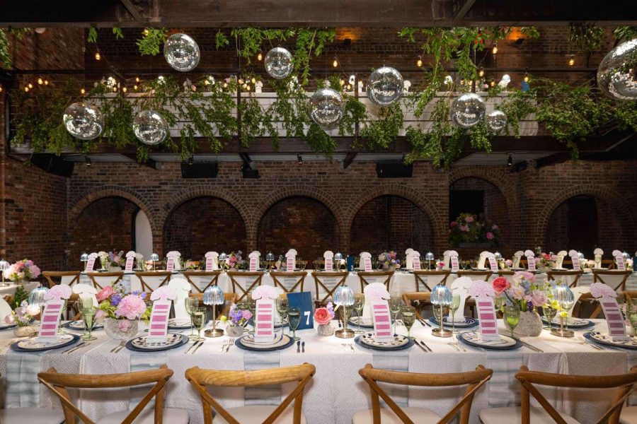 A photo of colorful indoor wedding reception featuring both colorful and lush green florals, along with String Lights and Multiple Disco Balls (Mirror Balls) hanging overhead at the Foundry in Long Island City, Queens, New York.