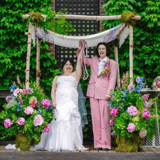 A couple wearing a white wedding dress and pink suit at their outdoor wedding ceremony at The Foundry in Long Island City, Queens, NY.