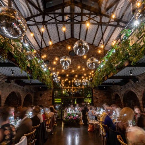 An indoor wedding reception featuring lush green florals, along with String Lights and Multiple Disco Balls (Mirror Balls) hanging overhead at the Foundry in Long Island City, Queens, New York.