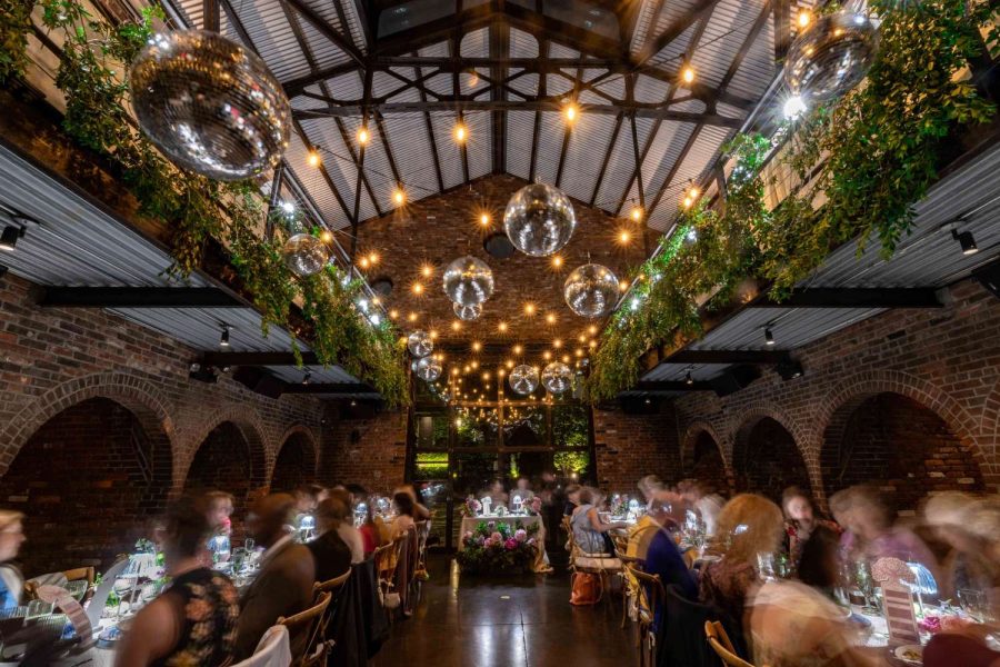 An indoor wedding reception featuring lush green florals, along with String Lights and Multiple Disco Balls (Mirror Balls) hanging overhead at the Foundry in Long Island City, Queens, New York.