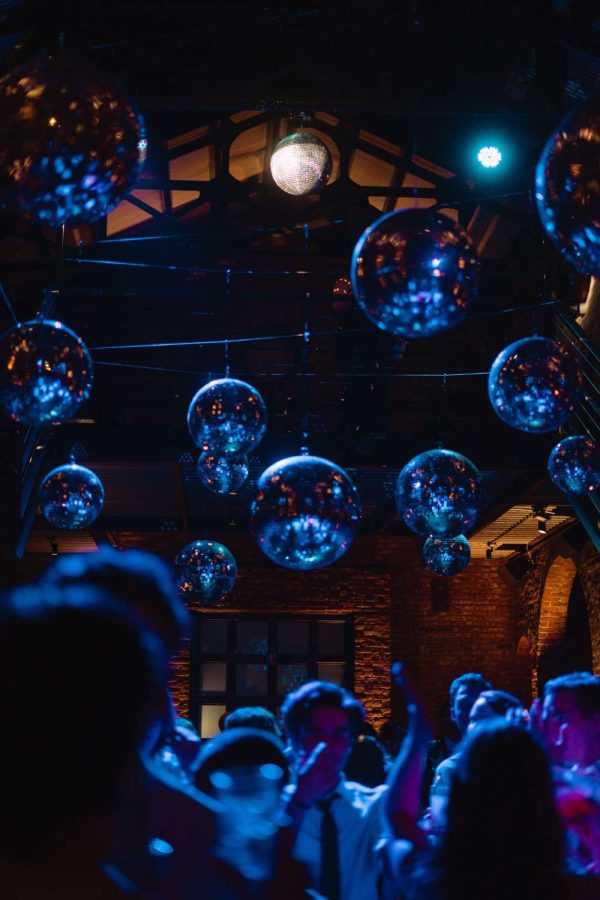 Guests are dancing in the main room under multiple mirror balls with a lavender color wash on the dance floor.