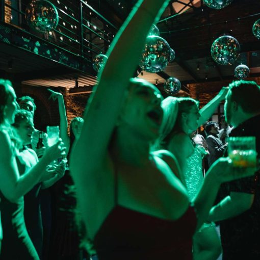 Guests are dancing in the main room under multiple mirror balls with a green color wash on the dance floor. Guests are dancing in the main room under multiple mirror balls with a green color wash on the dance floor.